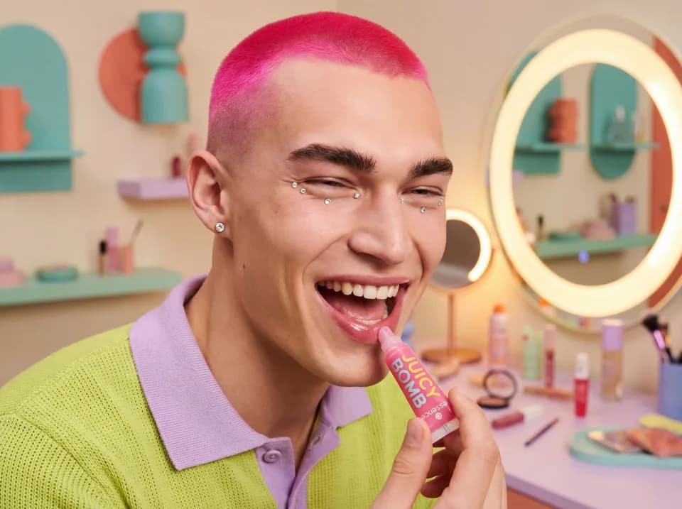 Person with pink hair applying lip balm in a bright room