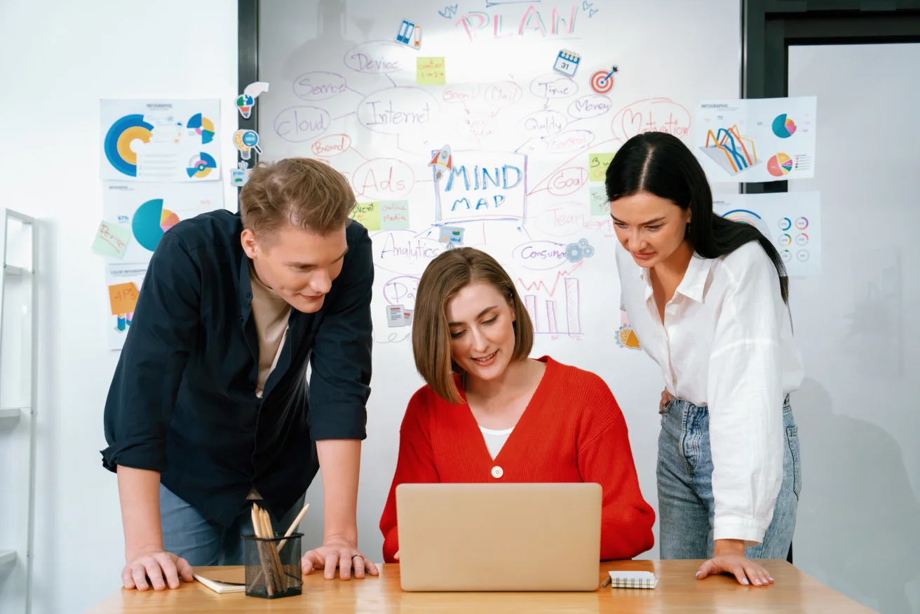Colleagues working together around a laptop in a bright office.