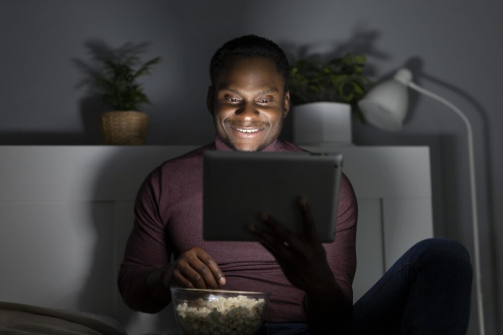 african american man watching streaming service indoors – VidAU.ai A man watching video on his phone after using the snapsave app for Facebook reel download
