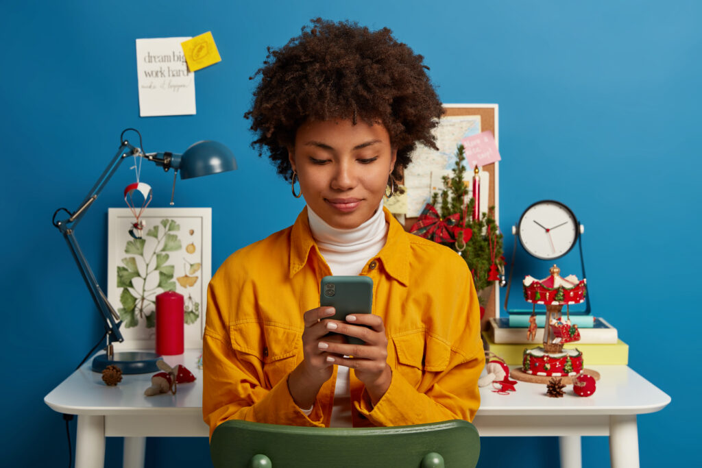 Pleased female student takes break from autodidact uses cellular for chatting online browses application sends text message checks mail via wifi sits on chair near workplace blue background how to write a product review