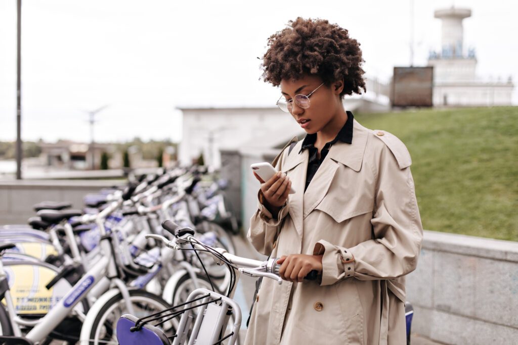 Woman holding a smartphone near parked bicycles, illustrating veed alternatives for mobile video editing on the go.